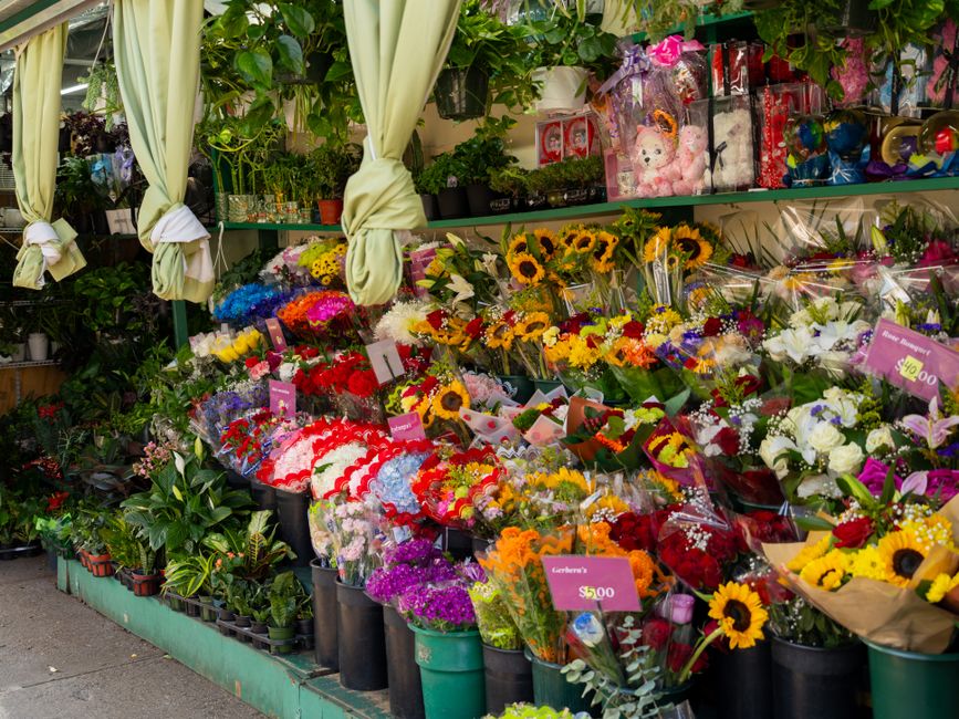 A vibrant flower stall at Lavender Hill, arranged with a wide variety of fresh floral bouquets, including sunflowers with bright yellow petals and dark centers, mixed seasonal blooms in shades of red,